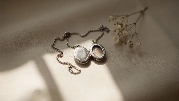 Two small silver lockets with intertwined chains resting on cream linen in soft light