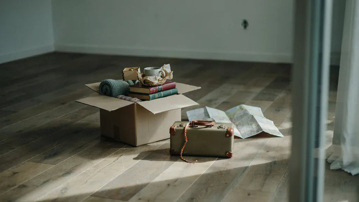 A packed moving box, a folded road map, and a friendship bracelet on a suitcase handle in warm afternoon light