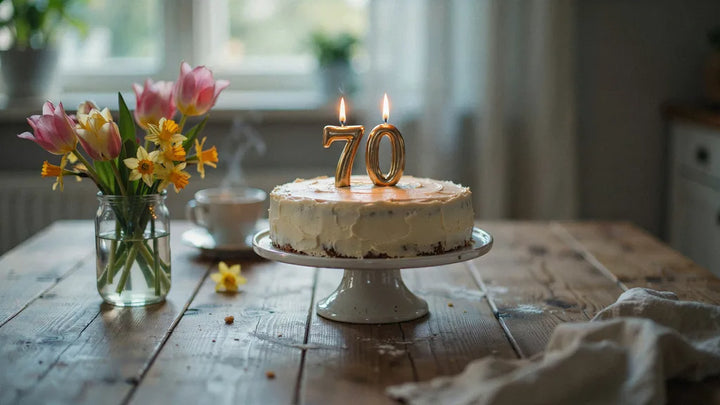 A birthday cake with number seventy candles surrounded by spring flowers in warm morning light