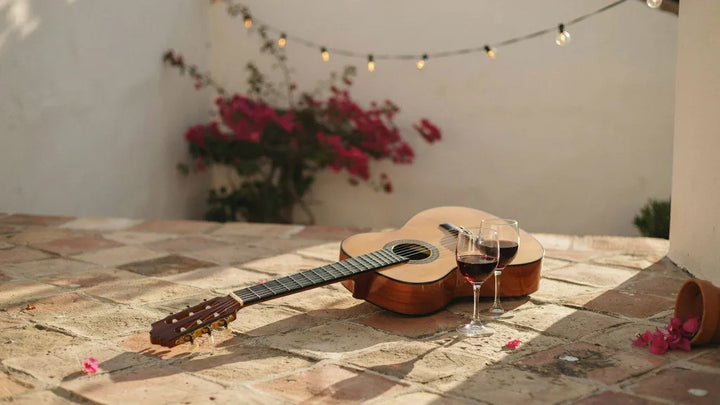 A classical Spanish guitar on a terracotta patio at golden hour beside two glasses of red wine