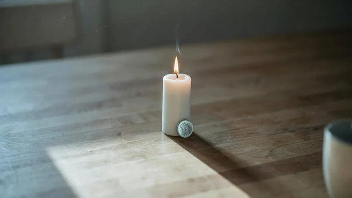 A single lit candle beside a small recovery chip on a plain wooden table in soft morning light