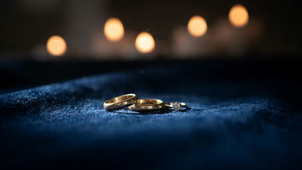 Two worn gold wedding bands and a diamond ring on blue velvet in warm candlelight