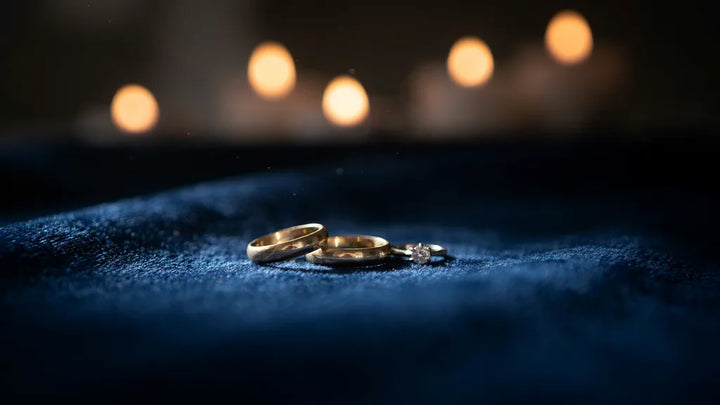 Two worn gold wedding bands and a diamond ring on blue velvet in warm candlelight