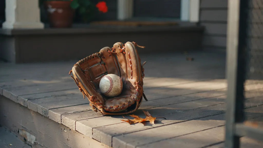 A worn leather baseball glove and ball resting on wooden porch steps in warm afternoon light