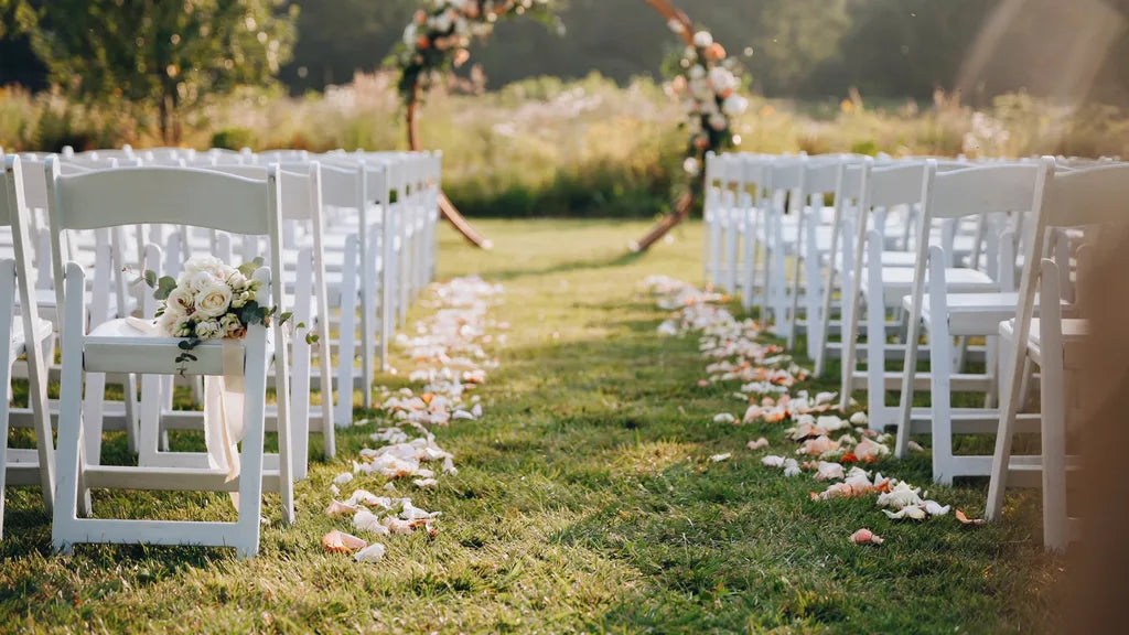 An empty wedding aisle lined with white chairs and rose petals, a bouquet on a front chair in golden light