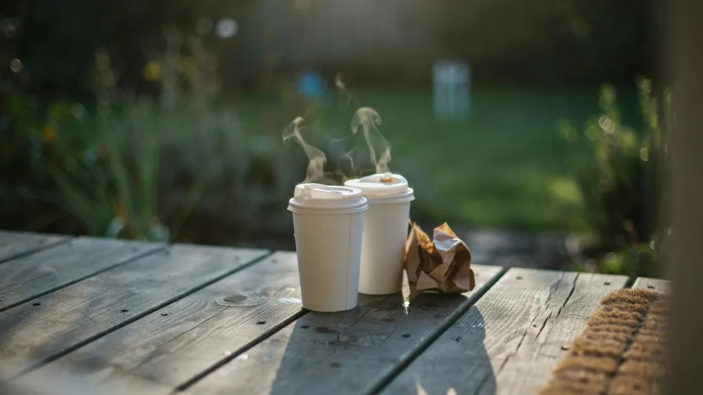 Two takeaway coffee cups left on a porch step in early morning light