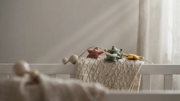 A knitted baby blanket beside a felt-star nursery mobile on a crib in soft morning light