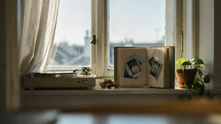 An old record player beside an open photo album on a windowsill in soft morning light