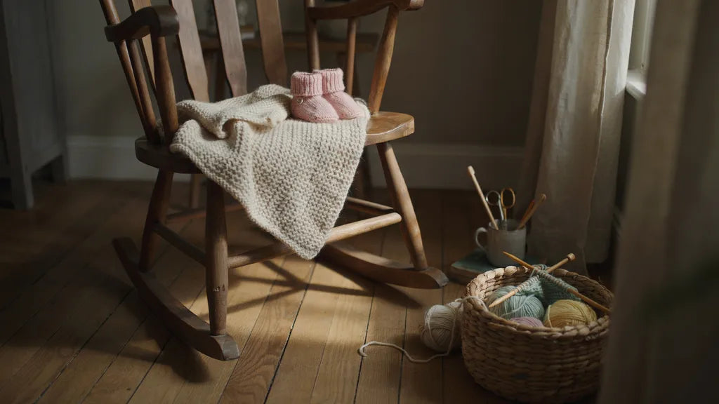 A hand-knitted baby blanket and tiny booties on a wooden rocking chair in warm light