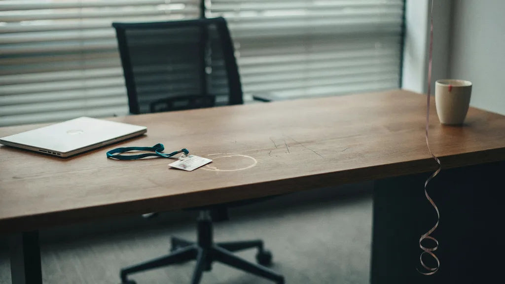 A cleared-out office desk with a faded coffee ring, a handed-in badge, and a balloon string at the edge