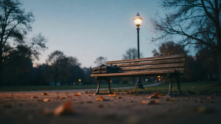 An empty park bench under a streetlight at dusk with a coat left on one end