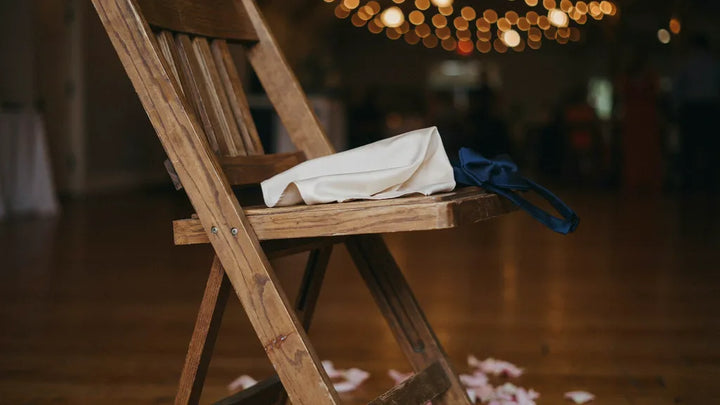 A loosened bow tie and folded pocket square on a wooden chair beside a wedding dance floor