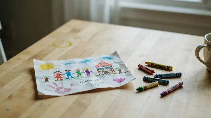 A child's crayon drawing and crayons on a wooden kitchen table in warm morning light
