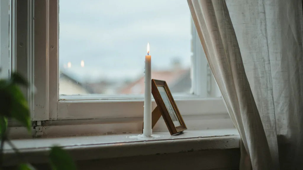 A lit memorial candle next to a small framed photo on a windowsill in soft light