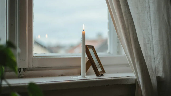 A lit memorial candle next to a small framed photo on a windowsill in soft light