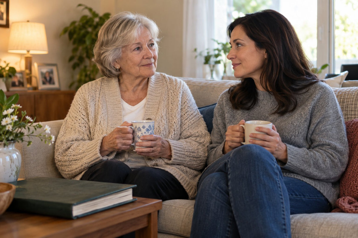 Two women quietly talking over mugs of tea on a sofa.