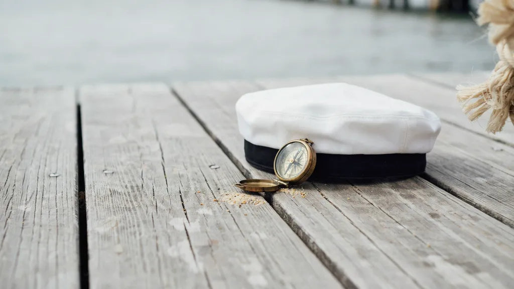 A white sailor's cap and brass compass on weathered dock wood — custom Navy tribute songs | Songbond