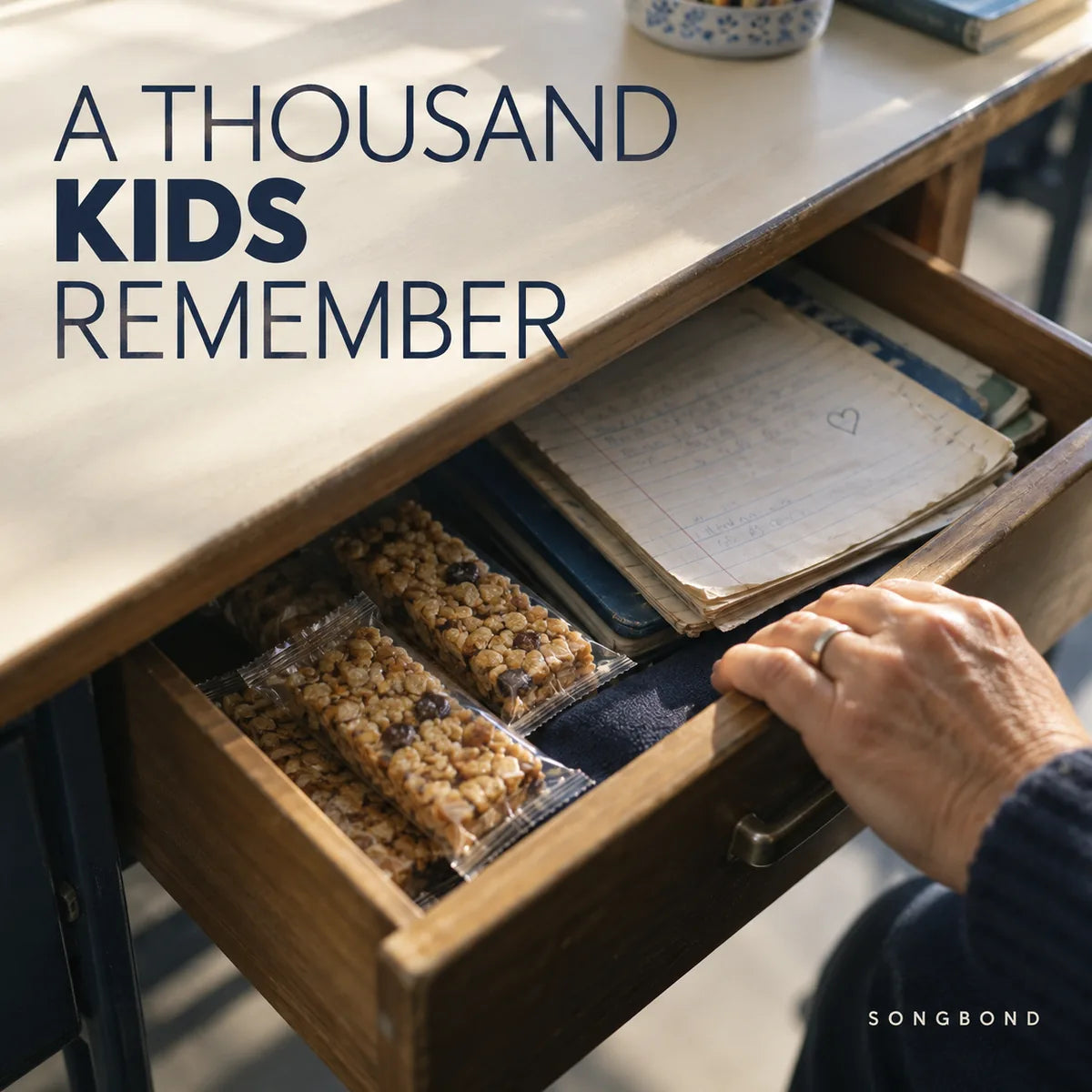 Music single cover for A Thousand Kids Remember by Songbond, showing an open desk drawer with granola bars, pupil notes and a teacher's hand.