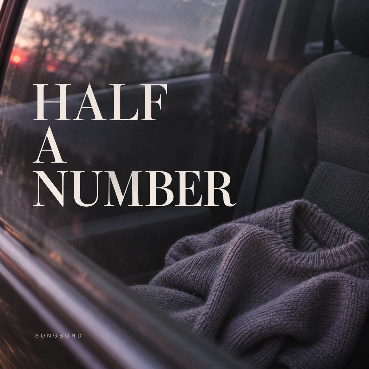 Music cover for Half a Number by Songbond, with a lilac-grey sweater on a car passenger seat through a softly reflected window beneath the cream title.