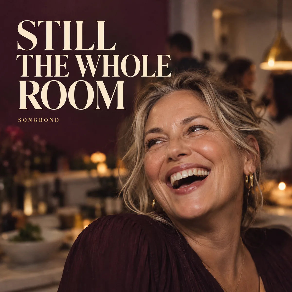 Music cover for Still The Whole Room by Songbond, with a mature woman laughing in warm kitchen light beside large cream lettering on a plum background.